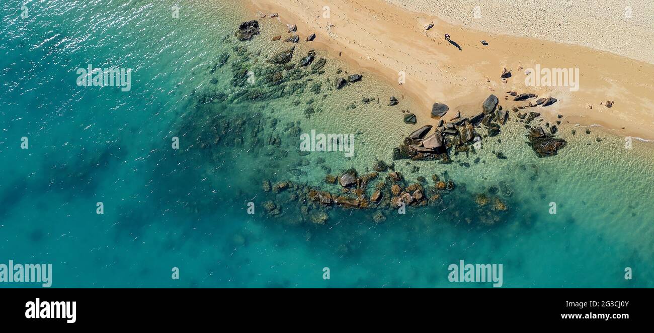 Rochers sur le rivage et sous l'eau dans un océan bleu étincelant à marée basse sur une plage de sable tropical Banque D'Images