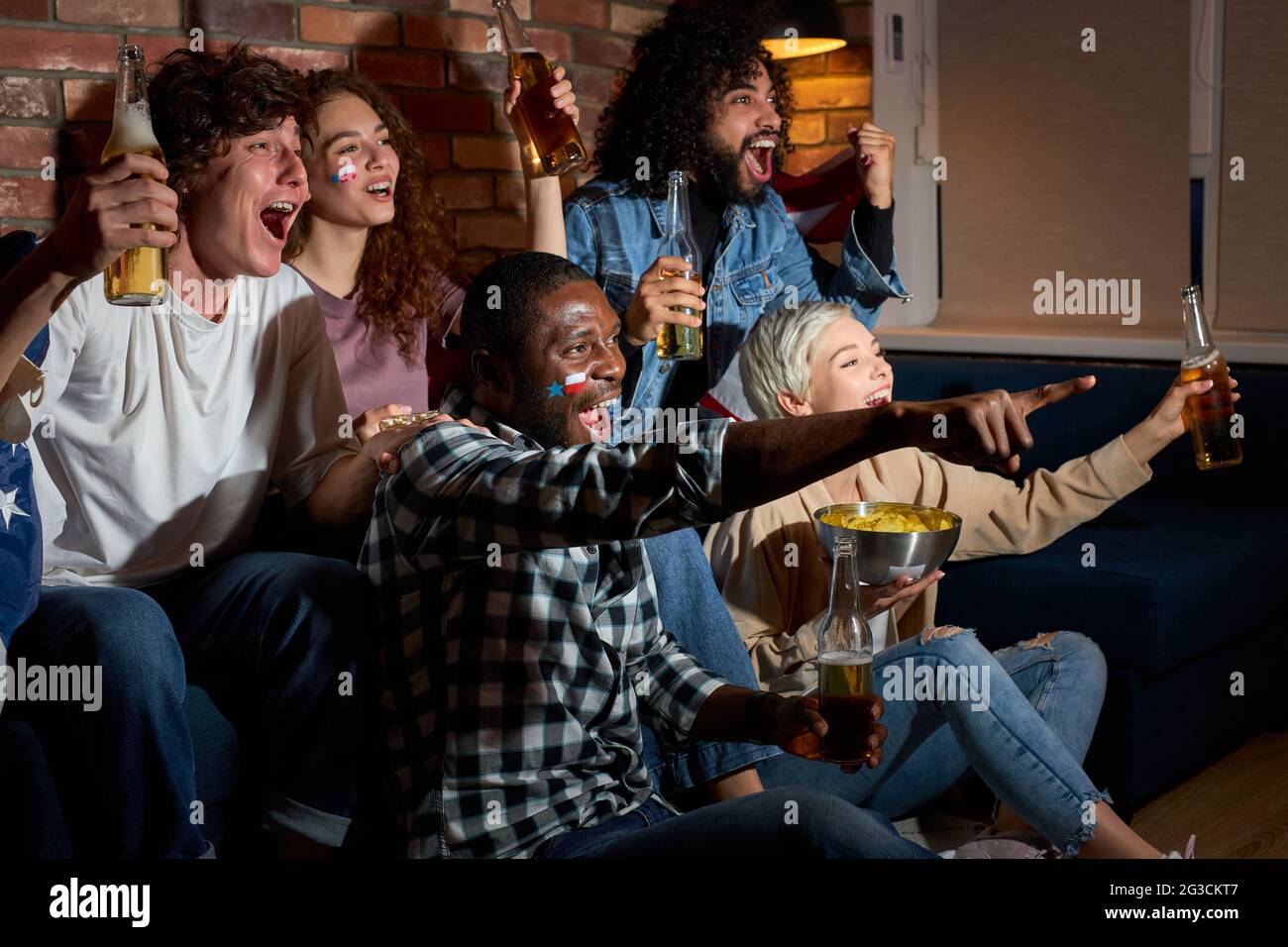 Groupe d'amis regardant la compétition sportive à la télévision ensemble, criant et criant par le bonheur, applaudissant à la maison dans la pièce sombre la nuit Banque D'Images