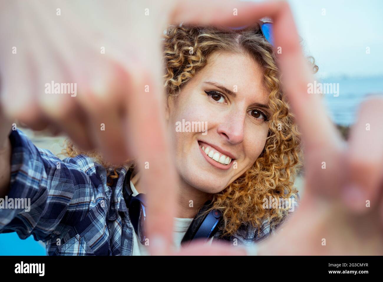 Gros plan portrait d'une jeune heureuse cheveux bouclés femme caucasienne regardant à travers un cadre fait de ses doigts. Capturez le concept du moment. Banque D'Images