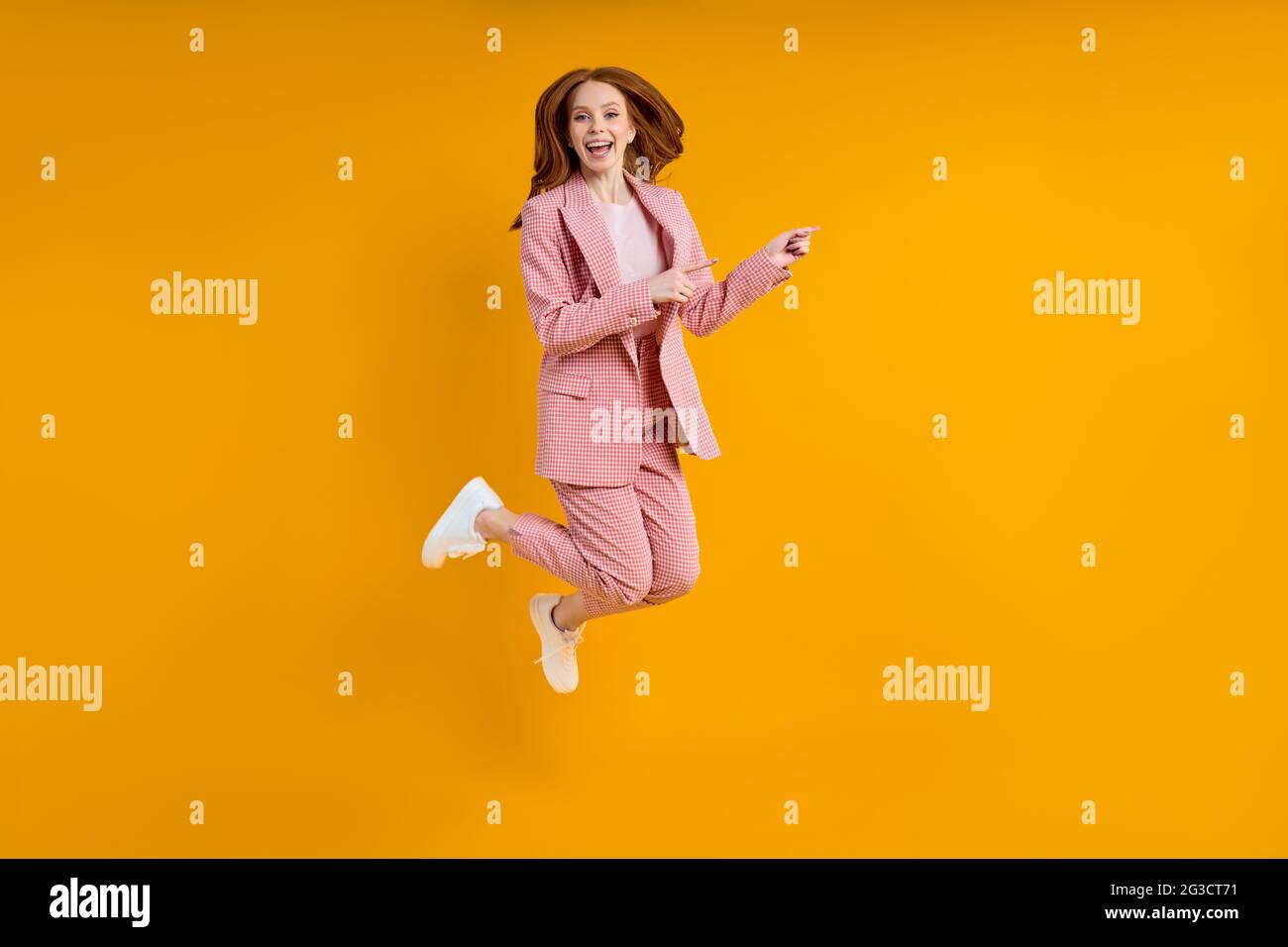 Femme d'affaires réussie en costume sautant doigt d'index sur le côté, isolé sur fond jaune, shopping. Portrait. Espace de copie Banque D'Images