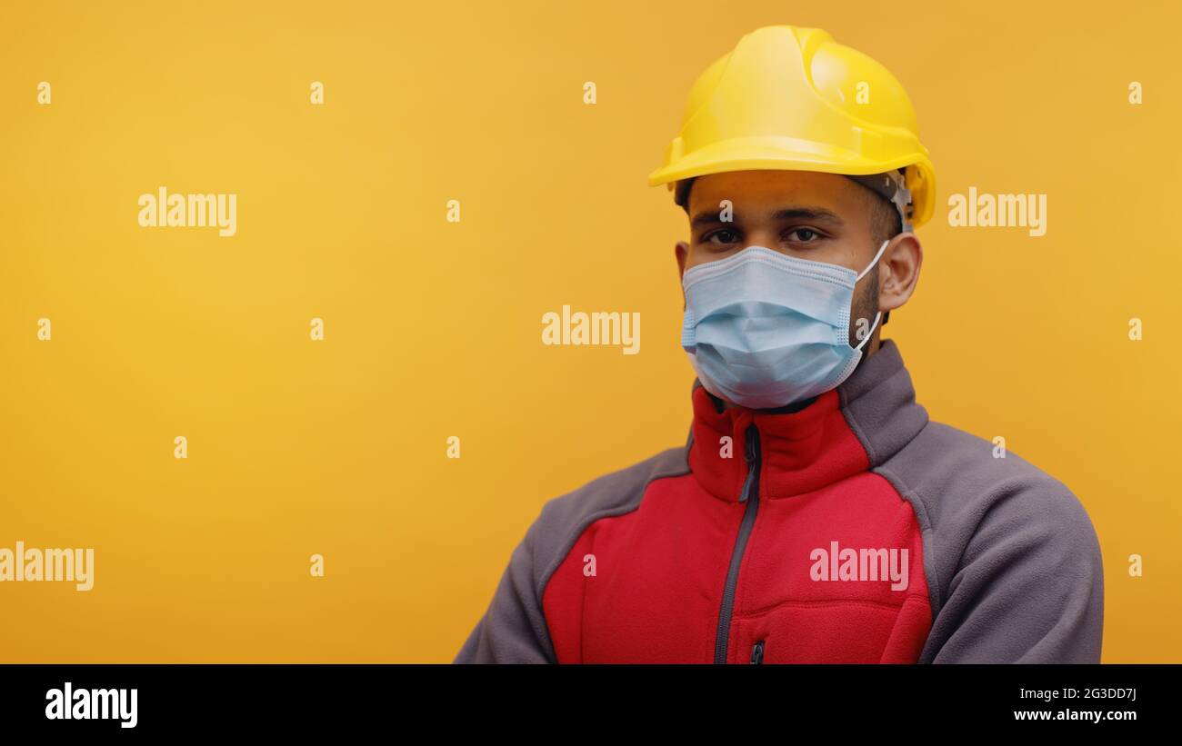 Portrait d'un jeune ingénieur indien portant un casque jaune de sécurité et un masque debout avec les bras croisés dans le studio avec fond jaune. Homme isolé. Gros plan. Banque D'Images