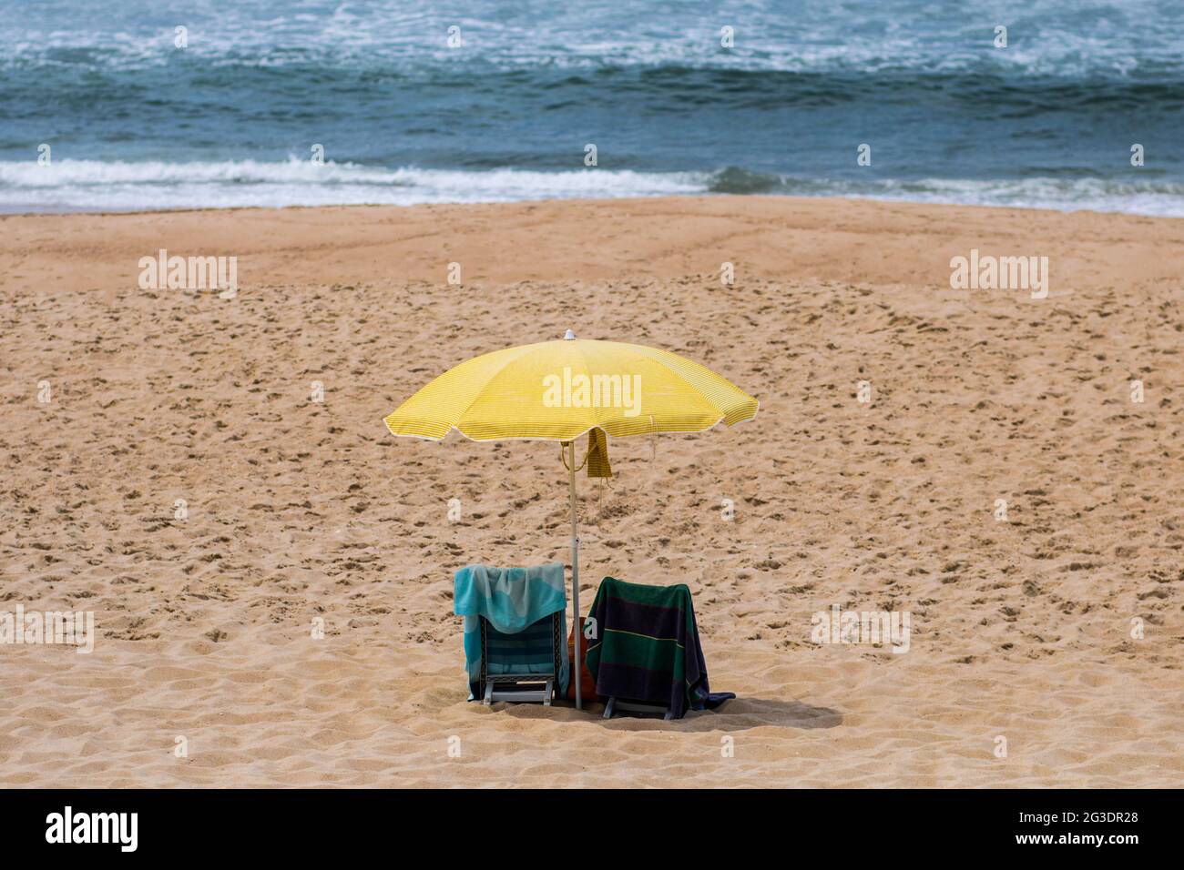 Parasol jaune avec deux chaises vides sur le sable d'une plage sauvage déserte à Quiaios, Portugal. Ouverture de la saison de baignade ou de vacances Banque D'Images