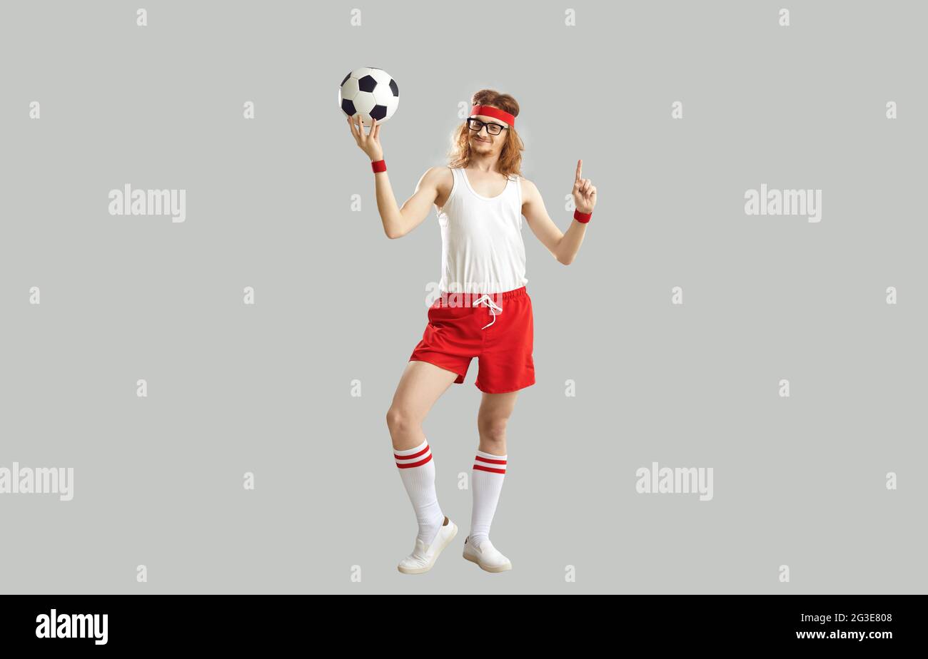 Drôle nerdy jeune homme en lunettes, débardeur, short et serre-tête tenant le ballon de football Banque D'Images
