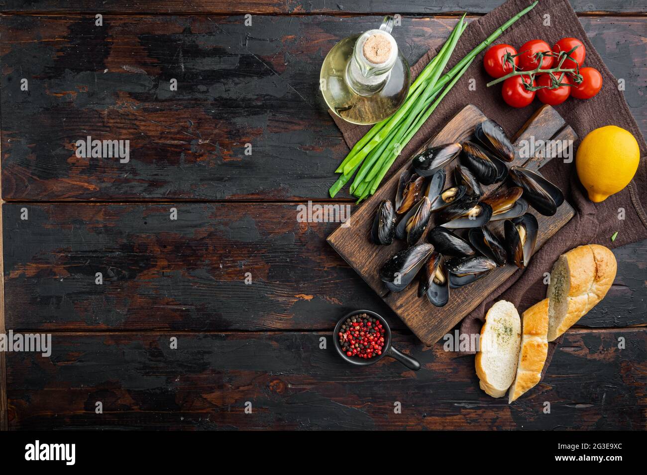 Moules cuites à la vapeur dans un décor de vin blanc, sur une planche à découper en bois, sur un arrière-plan de table en bois foncé, sur un plan de dessus, avec copyspace et espace pour le texte Banque D'Images