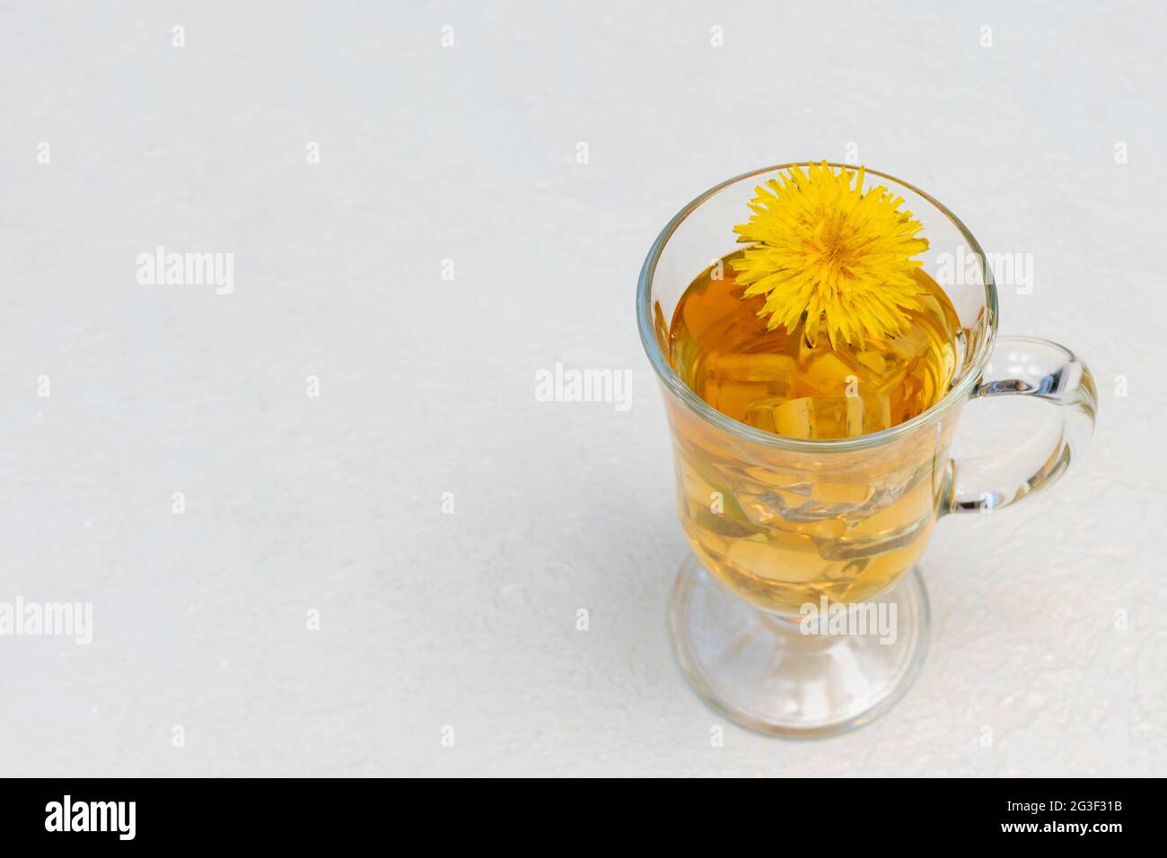 Thé de pissenlit à base de plantes saines dans une tasse de verre et fleur de pissenlit jaune à l'intérieur sur fond blanc, espace de copie, gros plan. Boisson rafraîchissante d'été, t Banque D'Images