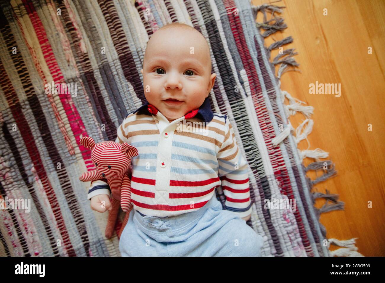 Par-dessus un bébé souriant mignon couché avec le jouet sur la moquette et regardant l'appareil photo Banque D'Images