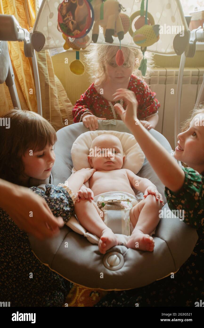 Grand angle de petites filles curieux se rassemblant autour de bébé doux tout en jouant ensemble à la maison Banque D'Images