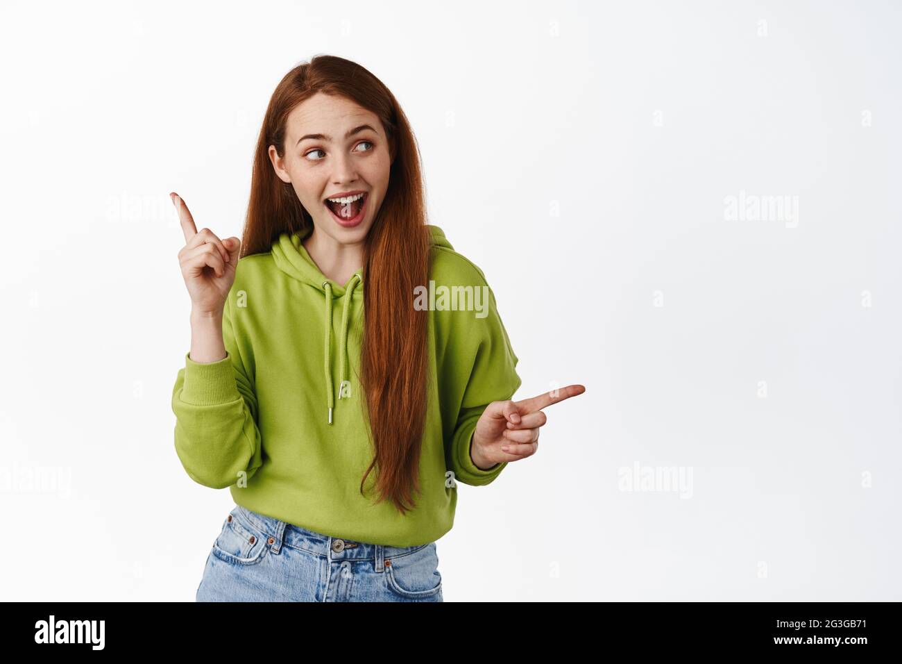 Joyeuse fête fille, redhead teen pointant latéralement, gauche et droit logo et sourire, rire et danse heureux, fond blanc Banque D'Images