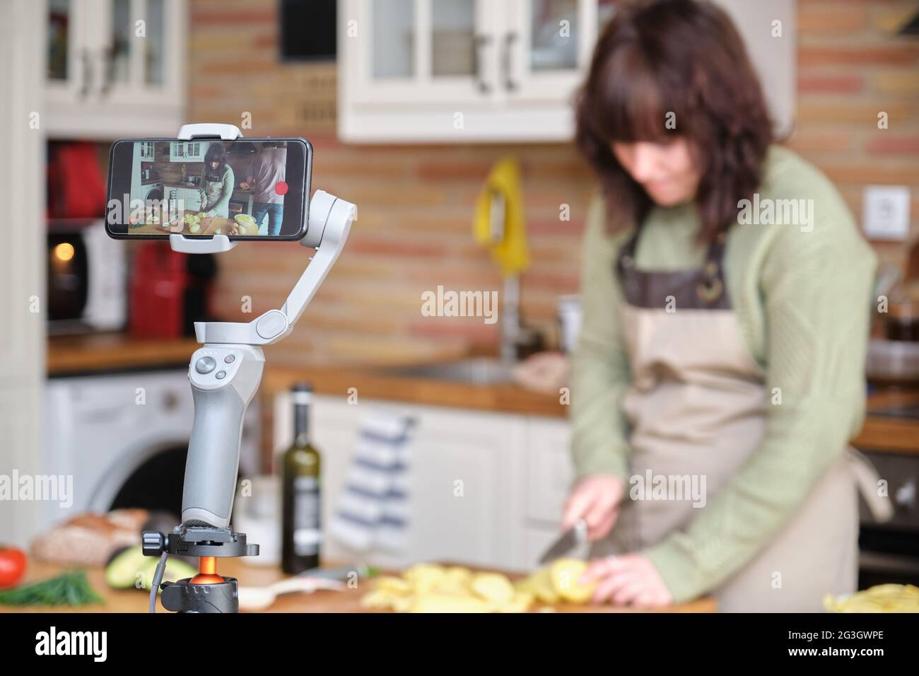 Une jeune femme coupe des pommes de terre et enregistre une vidéo avec son smartphone pour sa chaîne de cuisine. Créateur de contenu et influenceur. Banque D'Images
