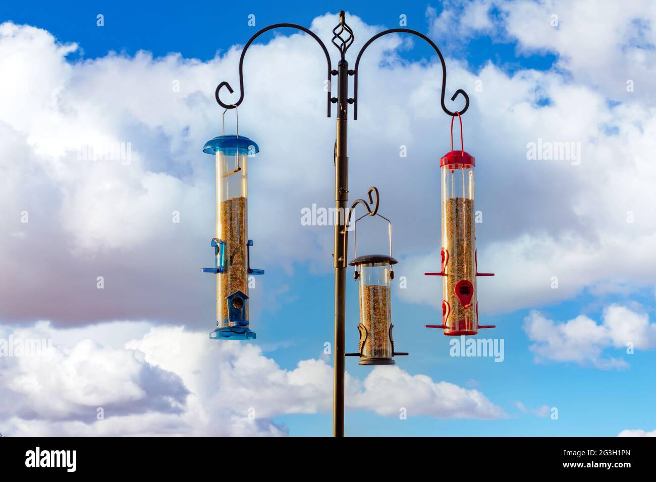 Trois mangeoires d'oiseaux accrochées à un poteau avec un fond de ciel de nuages Banque D'Images