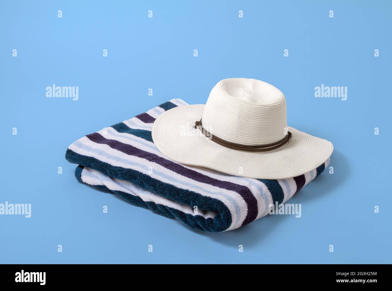 Grand chapeau blanc à visière pour femme sur une serviette de plage rayée avec un fond bleu clair Banque D'Images