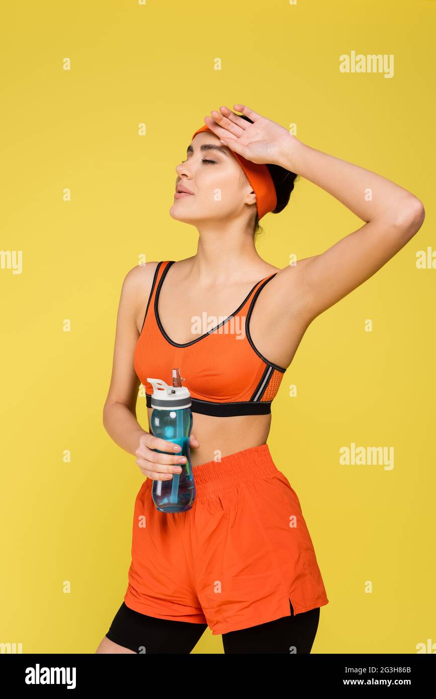 femme fatiguée avec bouteille de sport tenant la main près du visage isolé sur jaune Banque D'Images