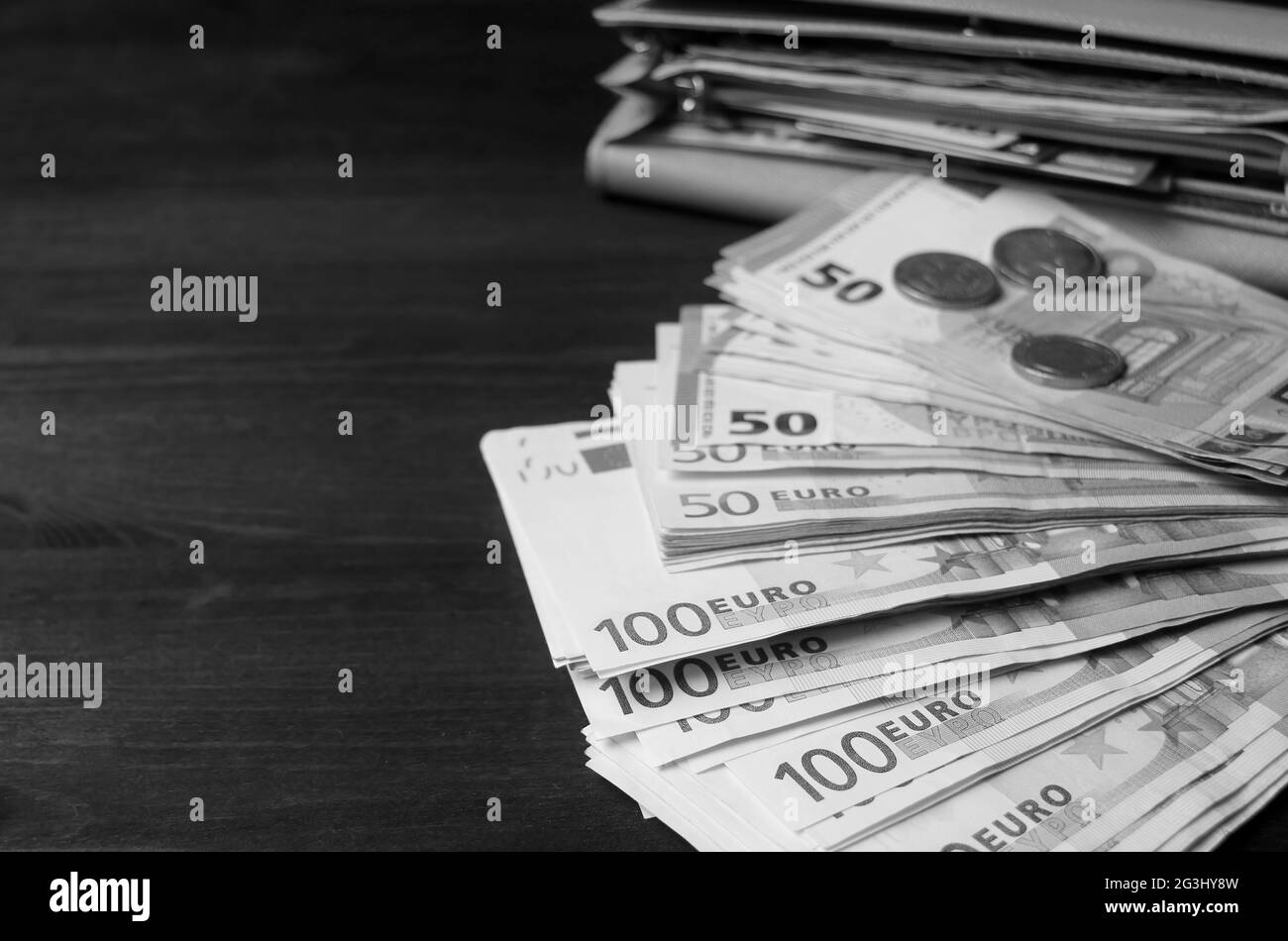 Image monochrome de petits pains de billets en euros avec pièces de monnaie floues et un portefeuille d'ouverture en toile de fond Banque D'Images