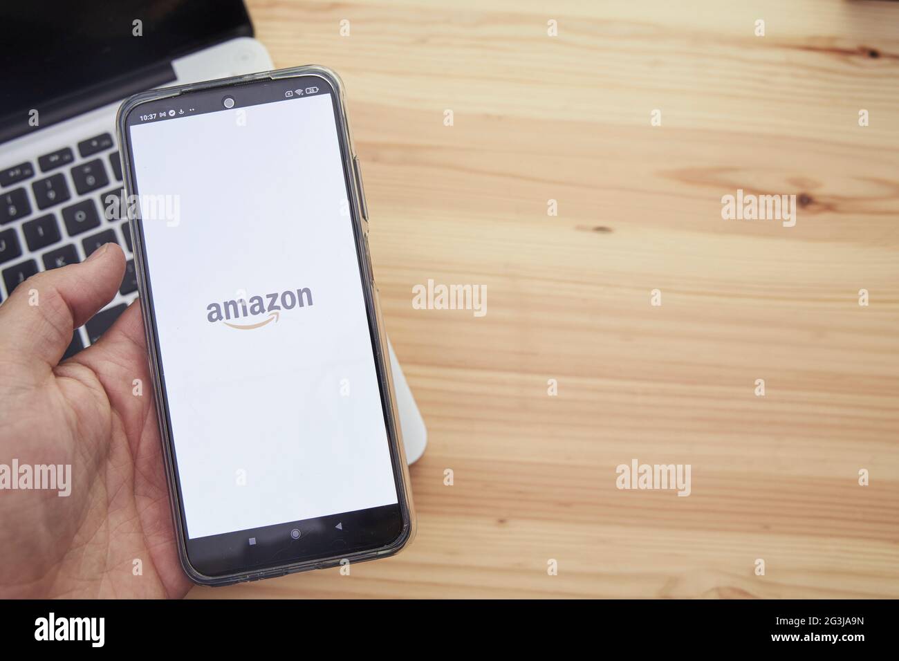 Madrid Espagne, juin 13 2021 ; mains tenant un appareil mobile intelligent avec le logo de l'application Amazon de la société sur l'écran et un ordinateur dans le Banque D'Images