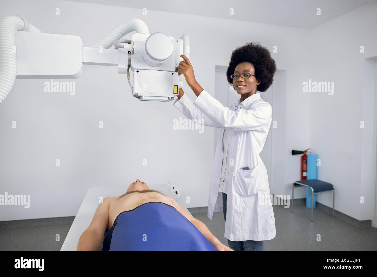 Souriante femme afro-américaine professionnelle médecin en uniforme posant  à la caméra, tout en prenant la radiographie thoracique d'un homme  caucasien patient. Radiographie des poumons et du squelette dans une  clinique moderne Photo