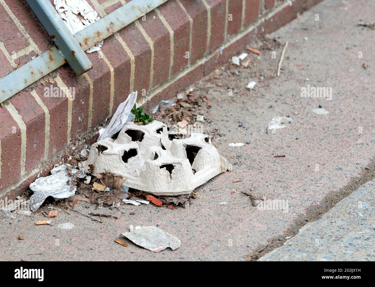 Petite pile de déchets sur le côté d'un trottoir. Pile est à côté d'un bâtiment en briques. L'un des morceaux est le carton utilisé pour transporter les tasses à café. Banque D'Images