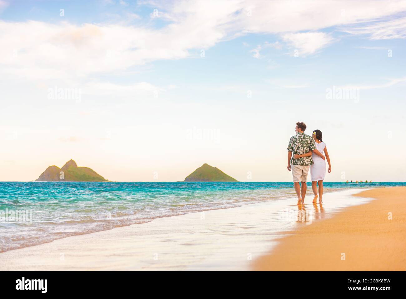 Hawaï vacances plage couple marchant au coucher du soleil luxe voyage destination lune de miel. Les jeunes mariés sont heureux sur la plage de Lanikai, Oahu, Hawaï. Banque D'Images