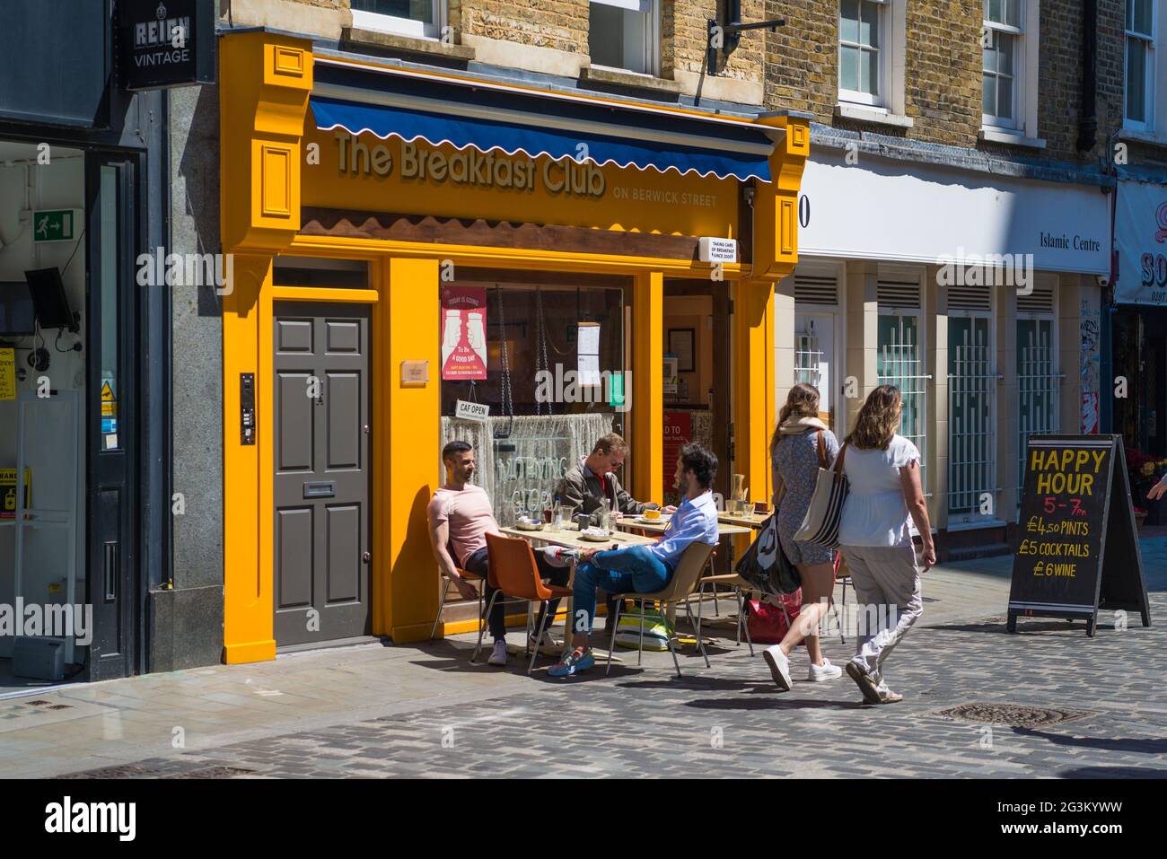 Des personnes assises aux tables de pavement et deux femmes marchant devant le Breakfast Club à Berwick Street, Soho, Londres, Angleterre, Royaume-Uni Banque D'Images