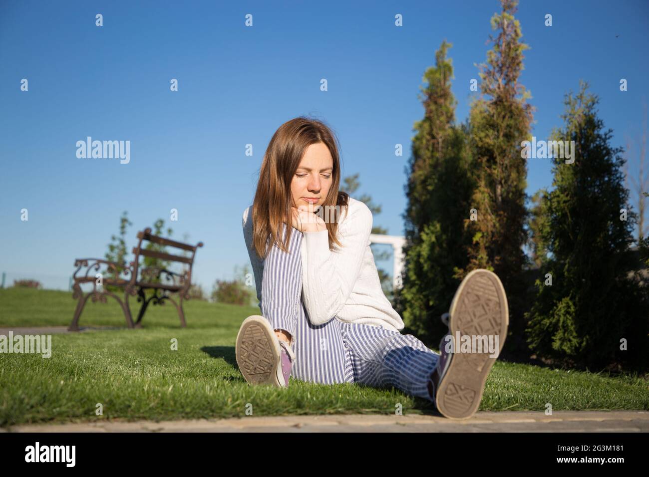 Une femme européenne de 30-40 ans est assise sur une pelouse verte dans un parc par une journée ensoleillée. Le visage exprime son inquiétude, la confusion, la réflexion sur les plans, s Banque D'Images