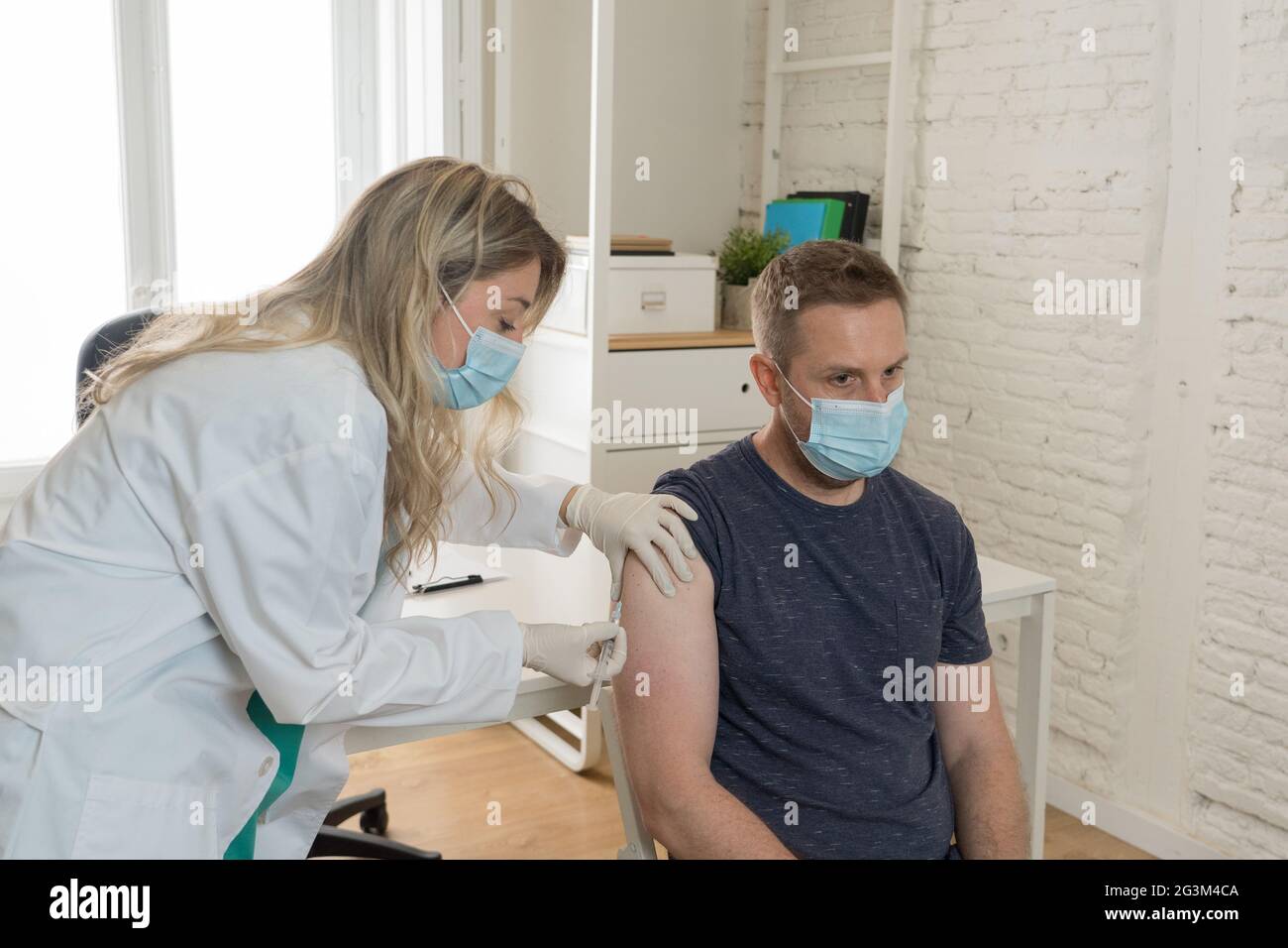 Femme médecin ou infirmière vaccinant un jeune homme en clinique. Homme patient se faire vacciner contre le coronavirus recevant le vaccin covid Inje intramusculaire Banque D'Images