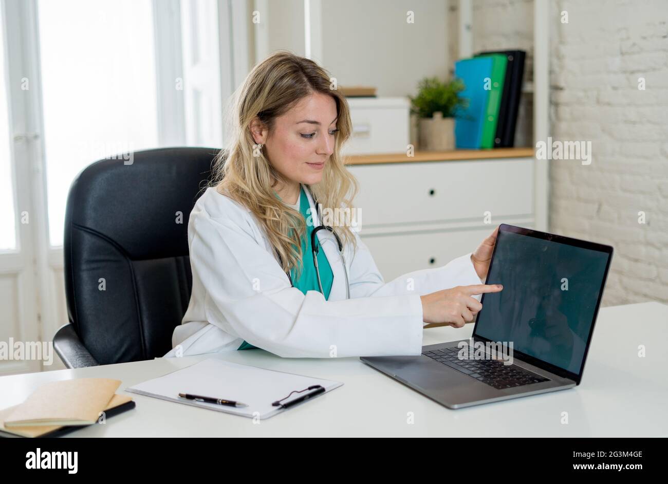 Portrait de femme heureuse attrayante médecin travaillant sur la paperasse, dossiers de patient et l'utilisation d'ordinateur portable pour la consultation en ligne assis sur la clinique ho Banque D'Images