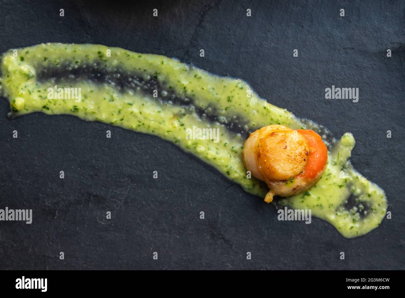 présentation gastronomique de pétoncles dans une sauce verte sur une assiette de pierre Banque D'Images