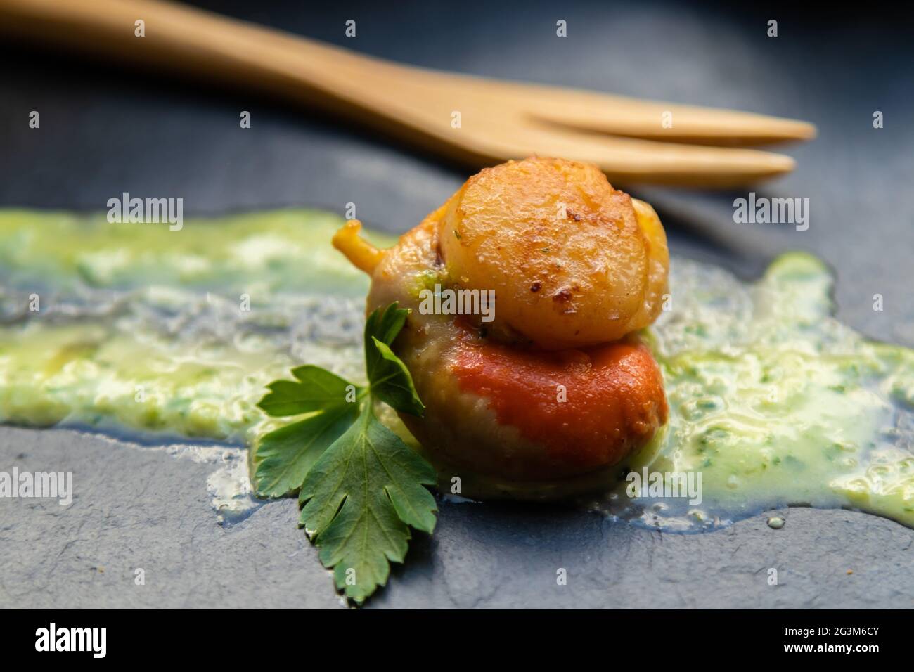 présentation gastronomique de pétoncles dans une sauce verte sur une assiette de pierre Banque D'Images