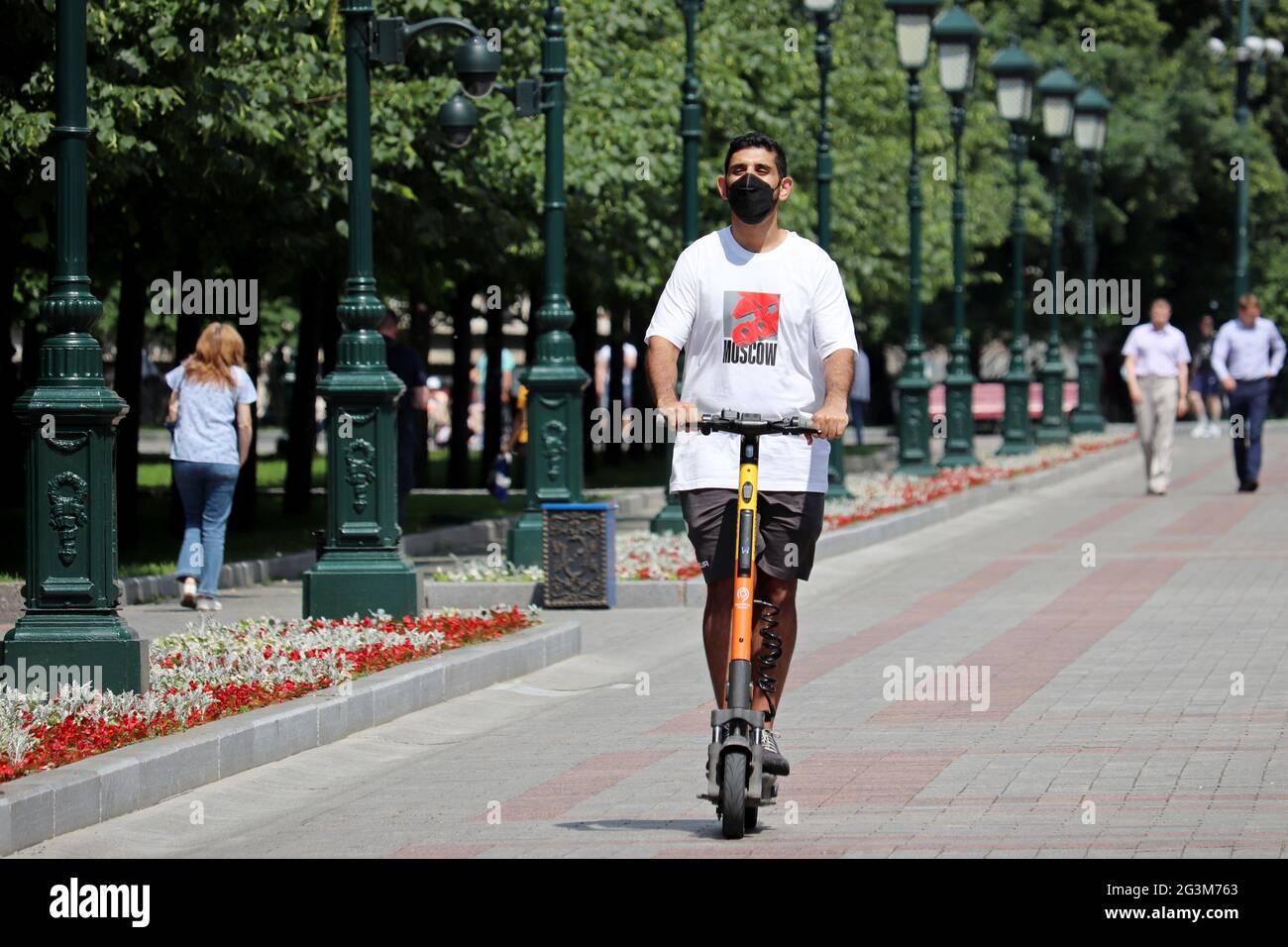 Guy dans le masque de protection du visage manèges un scooter électrique dans le jardin d'Alexander. Équitation en scooter électronique dans la ville d'été Banque D'Images