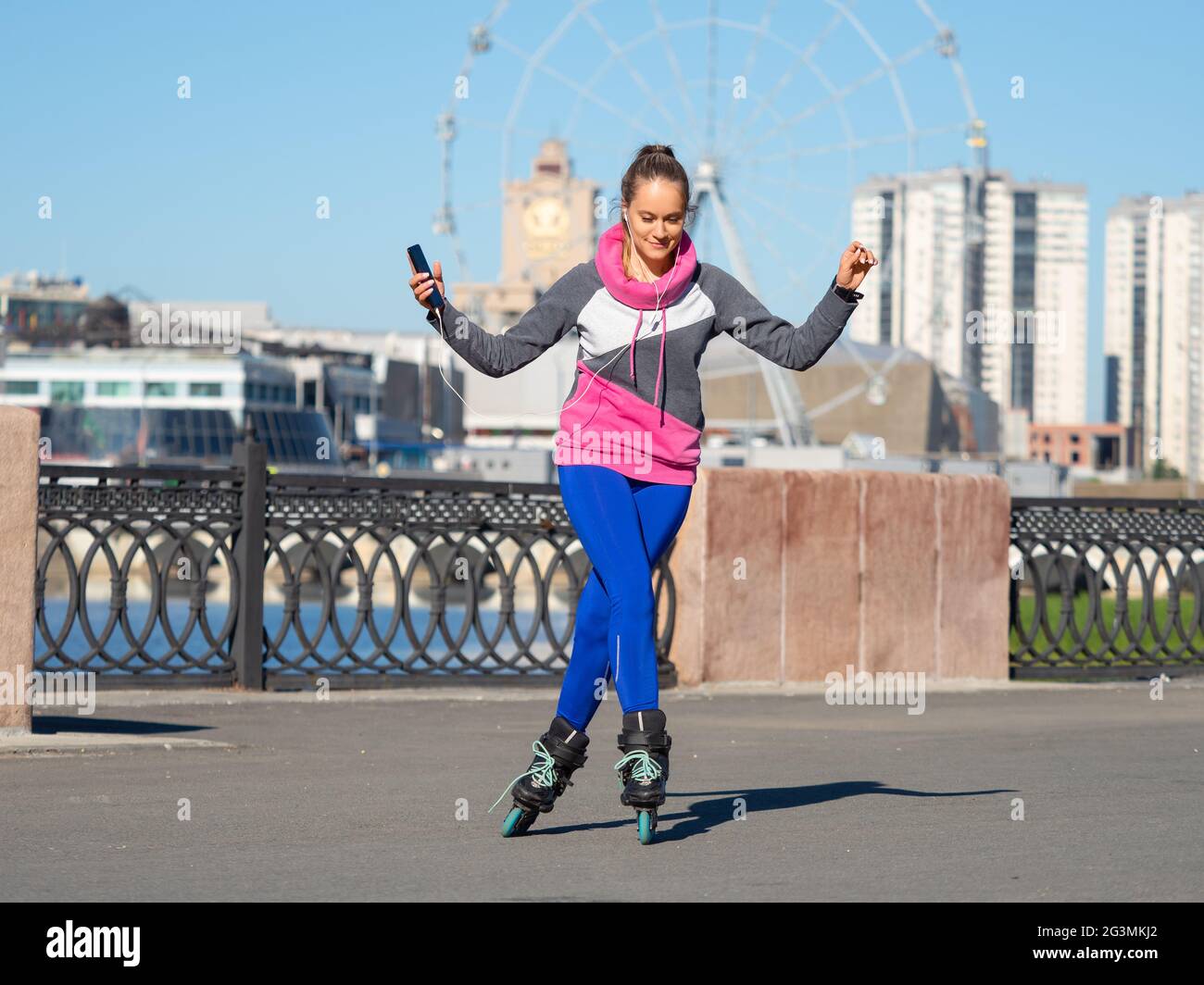 Une jeune femme est en train de faire du roller avec un smartphone dans ses mains et d'écouter de la musique à l'aide d'un casque. Elle se déplace à la musique et aime la vie. Banque D'Images