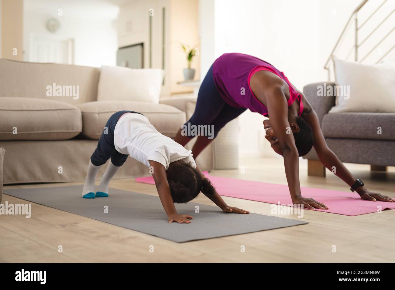 Mère et fille afro-américaines souriantes pratiquant le yoga, s'étendant sur des tapis dans la salle de séjour Banque D'Images
