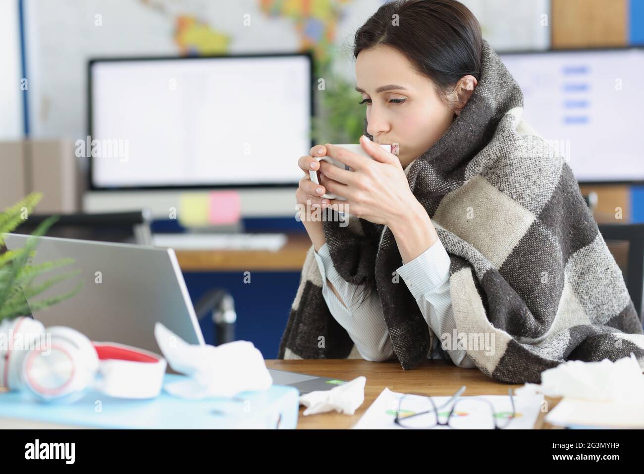 La jeune femme malade est assise dans une couverture chaude avec une tasse sur le lieu de travail Banque D'Images