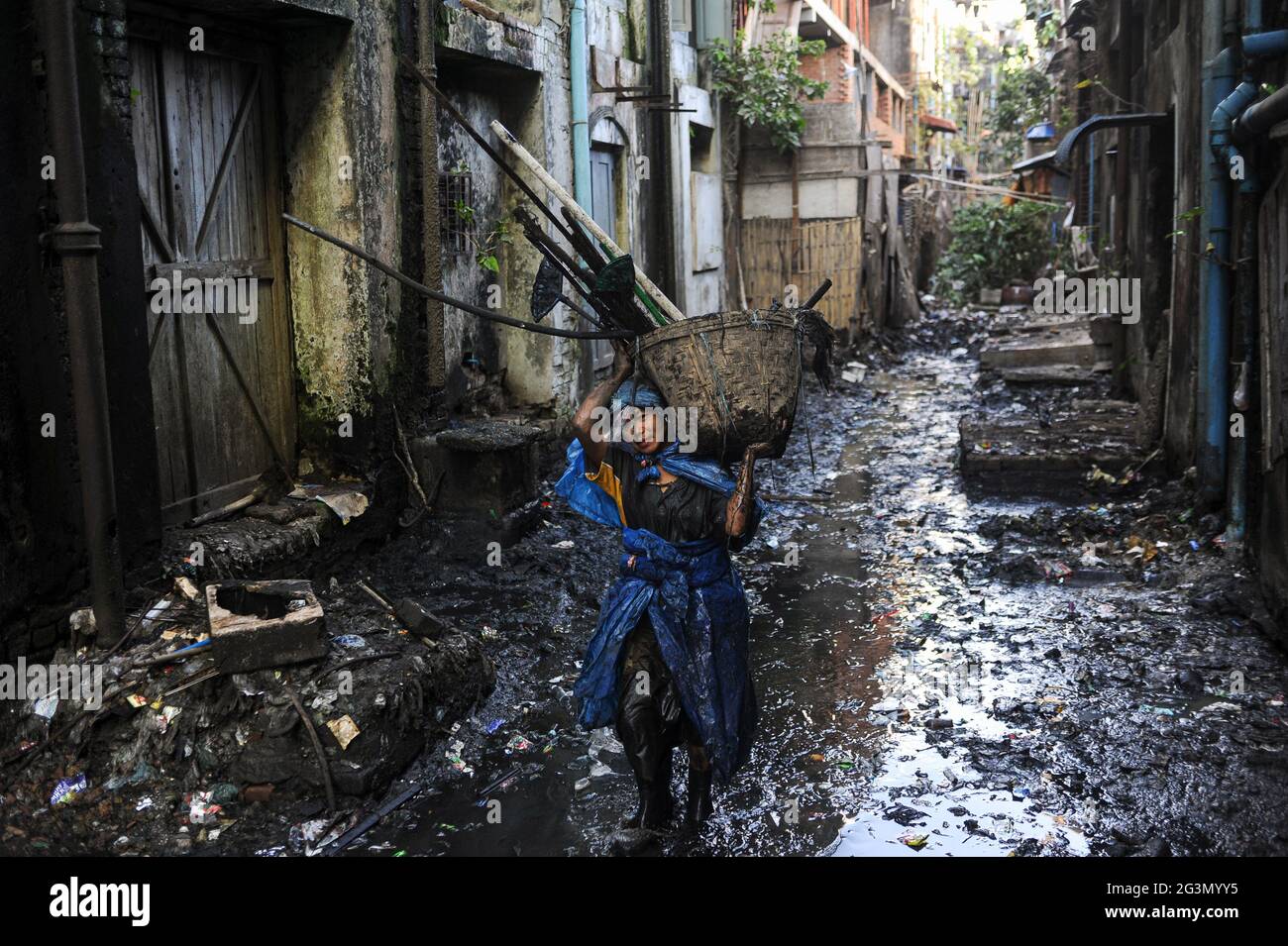 '19.02.2014, Yangon, , Myanmar - UNE femme nettoyant d'égout dans des vêtements de protection simples faits de sacs en plastique déchirés nettoyant l'égout ouvert obstrué de la ville Banque D'Images