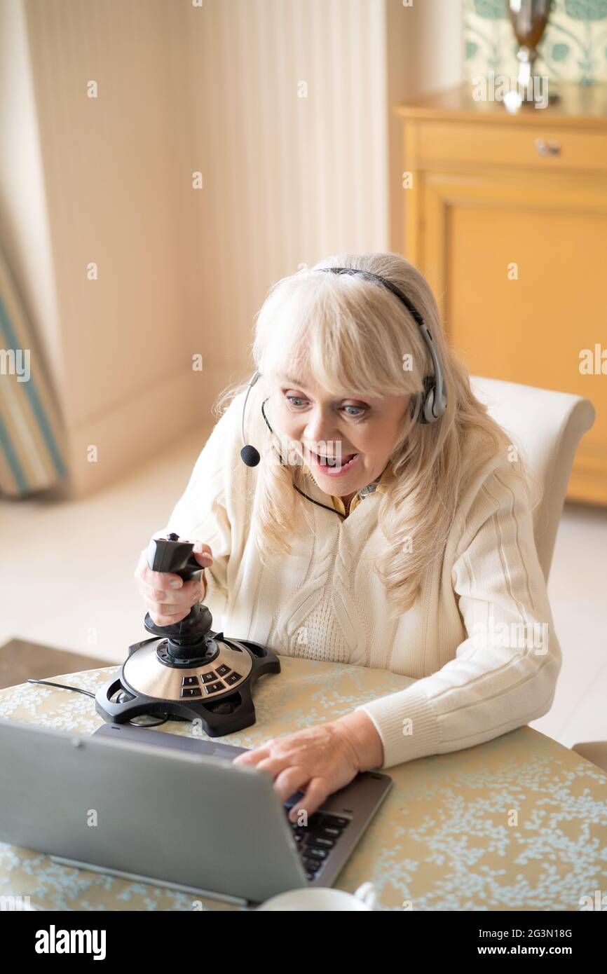 Une femme âgée joue à des jeux vidéo avec un joystick sur un ordinateur portable Banque D'Images