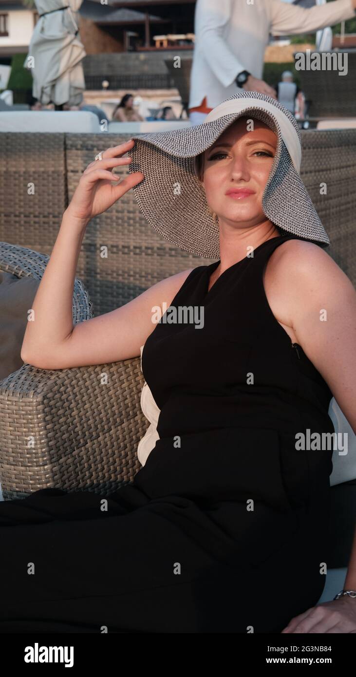 Europe de l'est Femme caucasienne d'âge moyen cheveux blond peau pâle teint pâle en robe noire chapeau de paille gris hors de l'été assis Banque D'Images