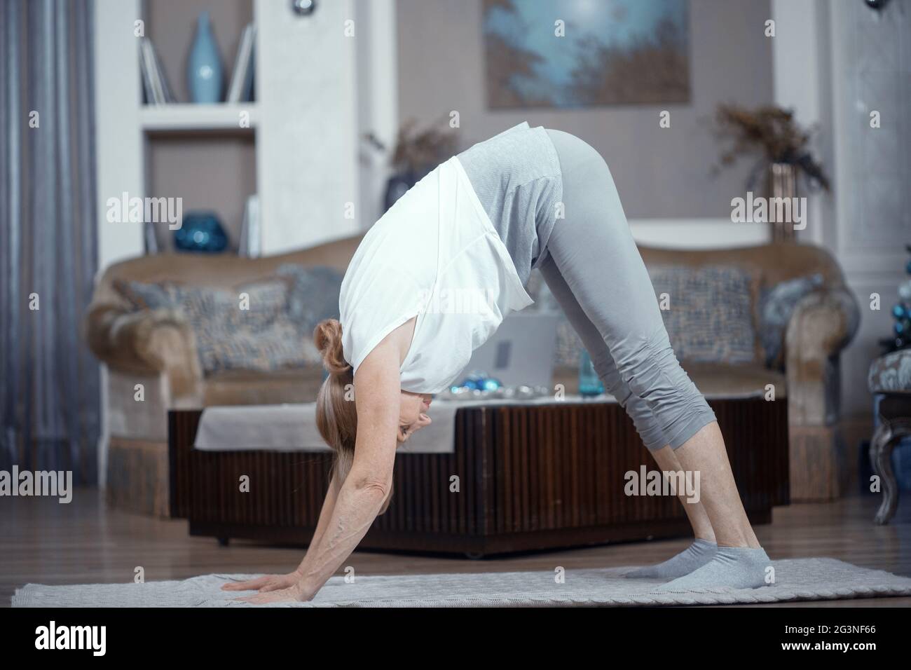Hot femme de plus de 50 ans faisant du yoga à la maison dans le salon. Banque D'Images