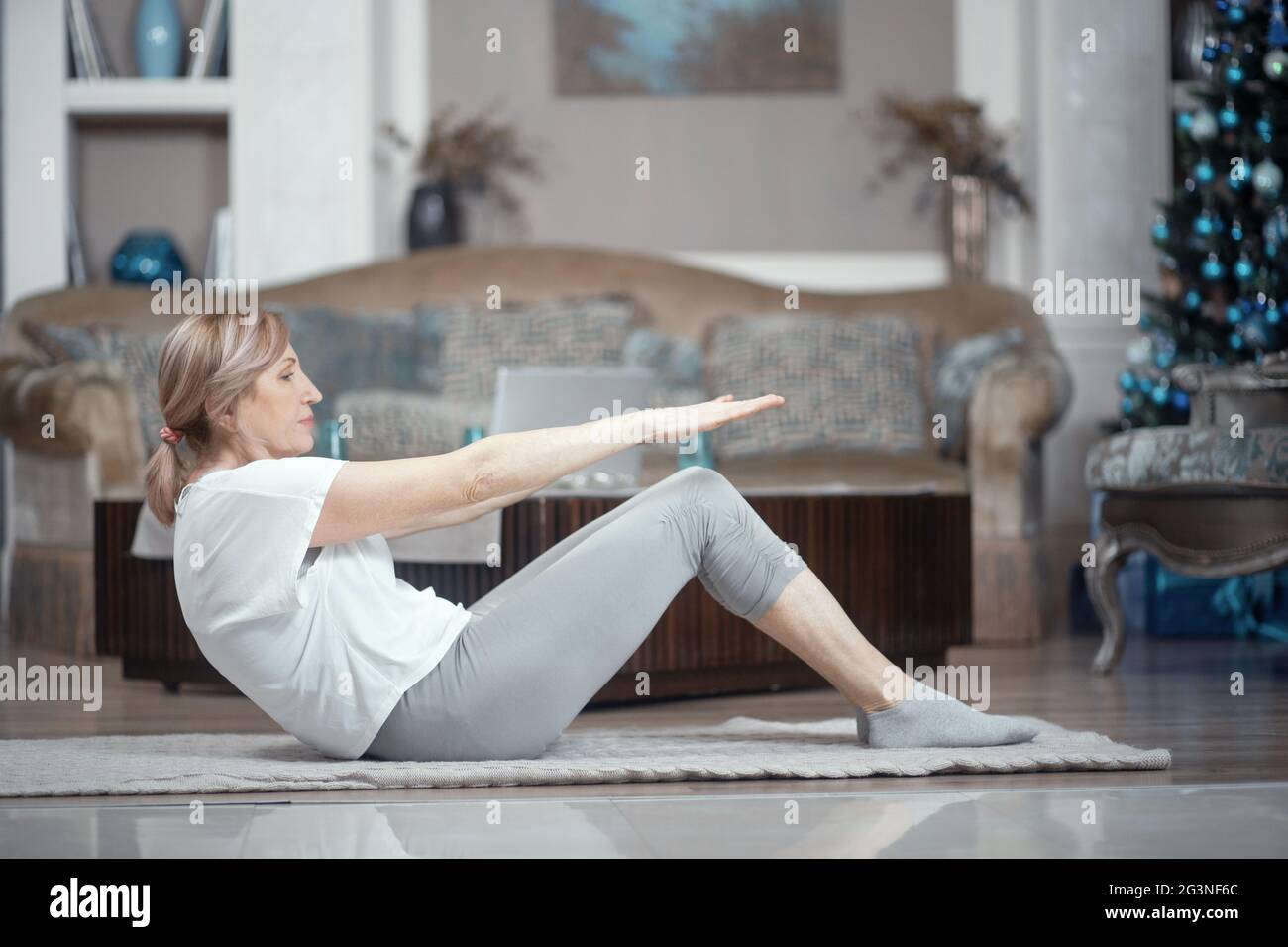 Hot femme de plus de 50 ans faisant du yoga à la maison dans le salon. Banque D'Images