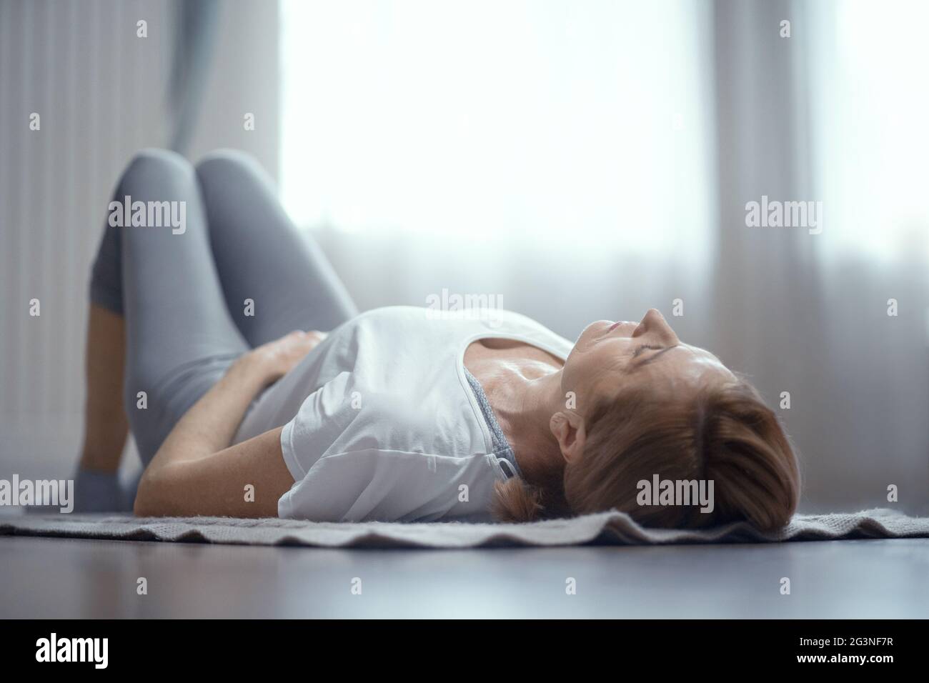 Hot femme de plus de 50 ans faisant du yoga à la maison dans le salon. Banque D'Images