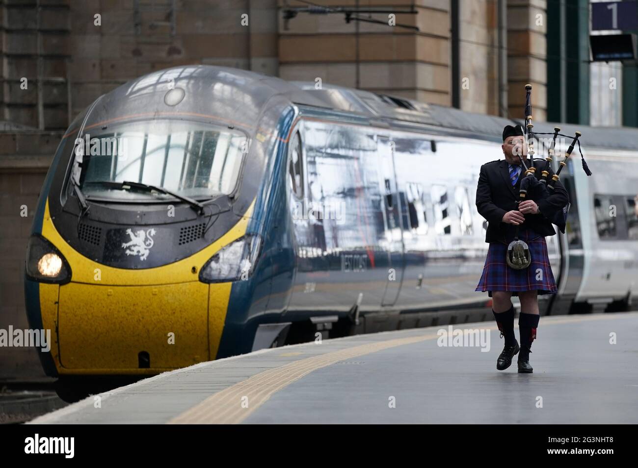 Un joueur de cornemuse parcourt la plate-forme le long du train Avanti West Coast Class 390 EMU qui arrive à la gare centrale de Glasgow depuis Londres Euston, sans avoir réussi à battre le record de 36 ans pour le trajet le plus rapide entre Londres et Glasgow. Le train Royal Scot est arrivé à Glasgow Central 21 secondes après le record de trois heures, 52 minutes et 40 secondes établi par British Rail en décembre 1984 Date de la photo : jeudi 17 juin 2021. Banque D'Images