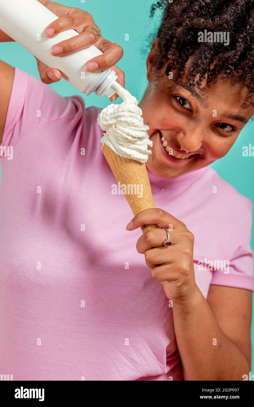 Fille noire mangeant un cône de crème glacée sur un fond turquoise Banque D'Images