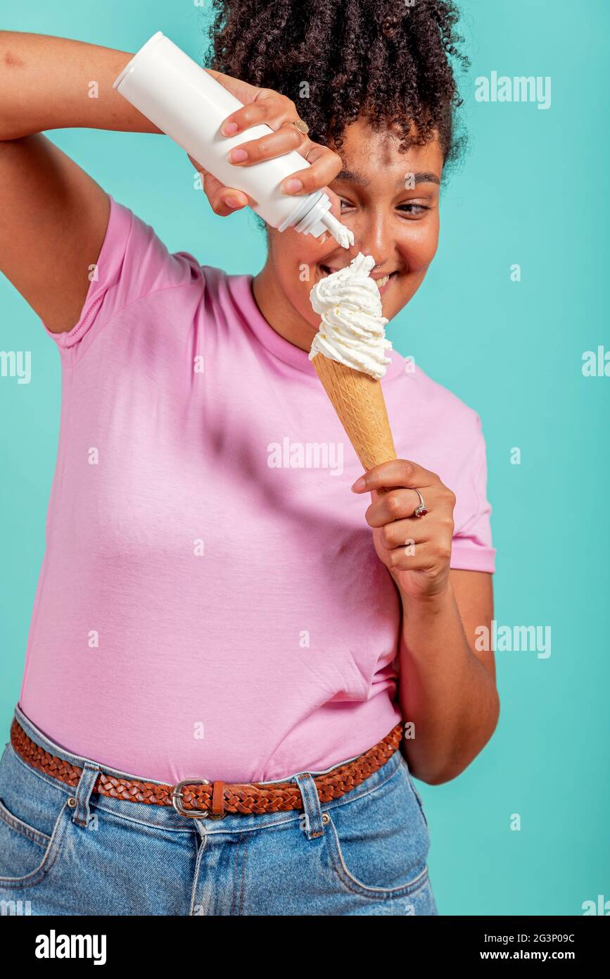 Fille noire mangeant un cône de crème glacée sur un fond turquoise Banque D'Images