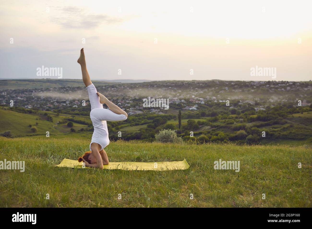 Fille debout sur la tête sur le tapis de fitness et pratiquant le yoga sur la nature à l'extérieur Banque D'Images