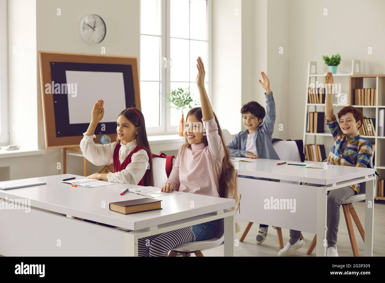 Un groupe d'élèves du primaire lève la main en classe pour répondre aux questions de l'enseignant. Banque D'Images