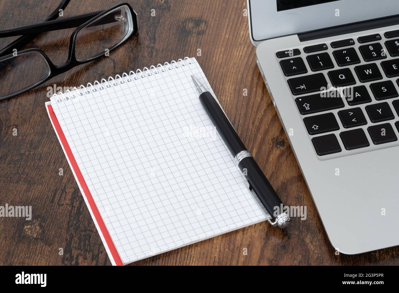 bloc-notes en spirale vierge et stylo avec papier quadrules à côté de l'ordinateur portable sur une table en bois Banque D'Images