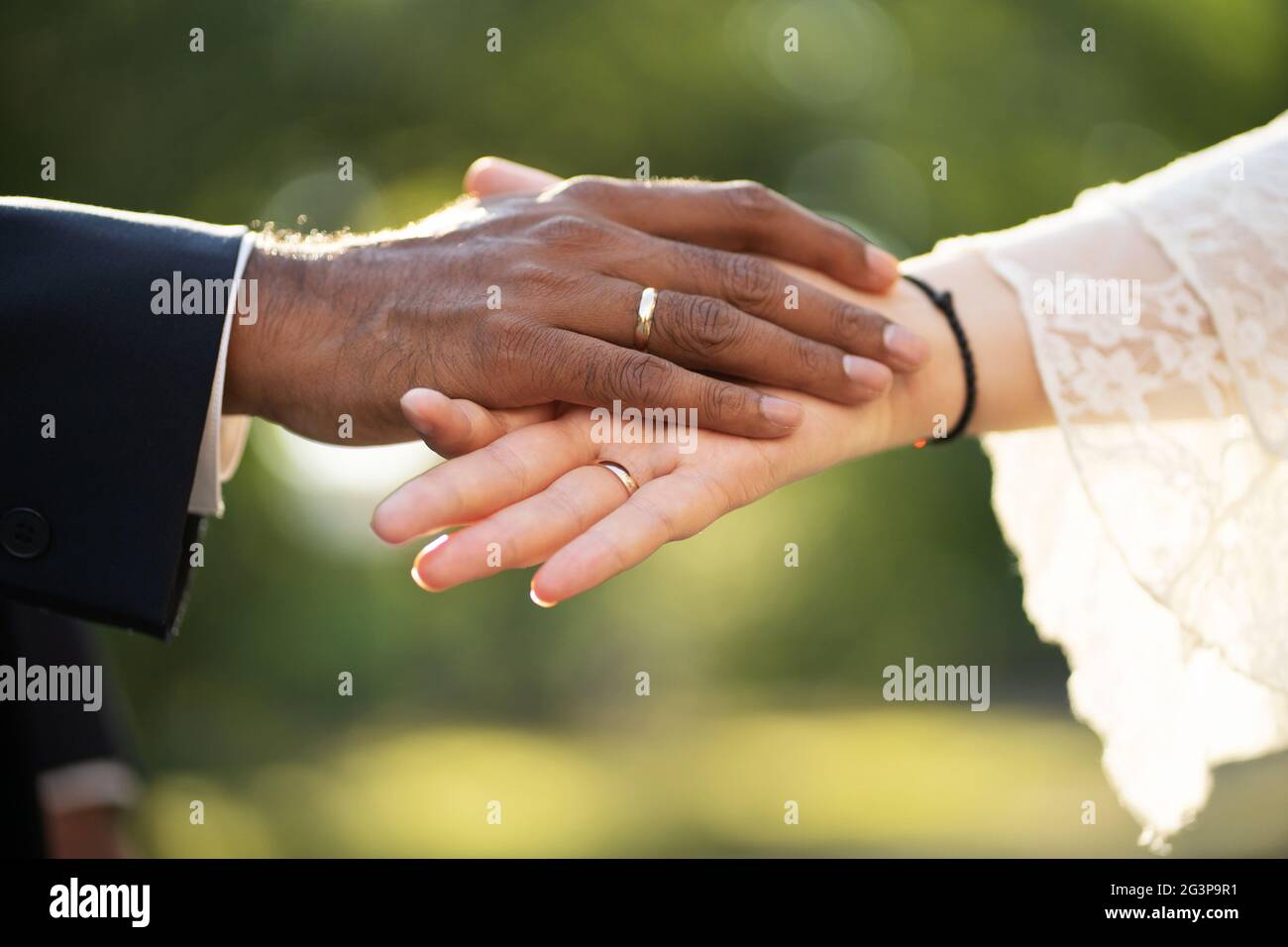 Les mains d'un marié à la peau sombre et d'une mariée à la peau claire avec des anneaux se touchent doucement vue rapprochée Banque D'Images