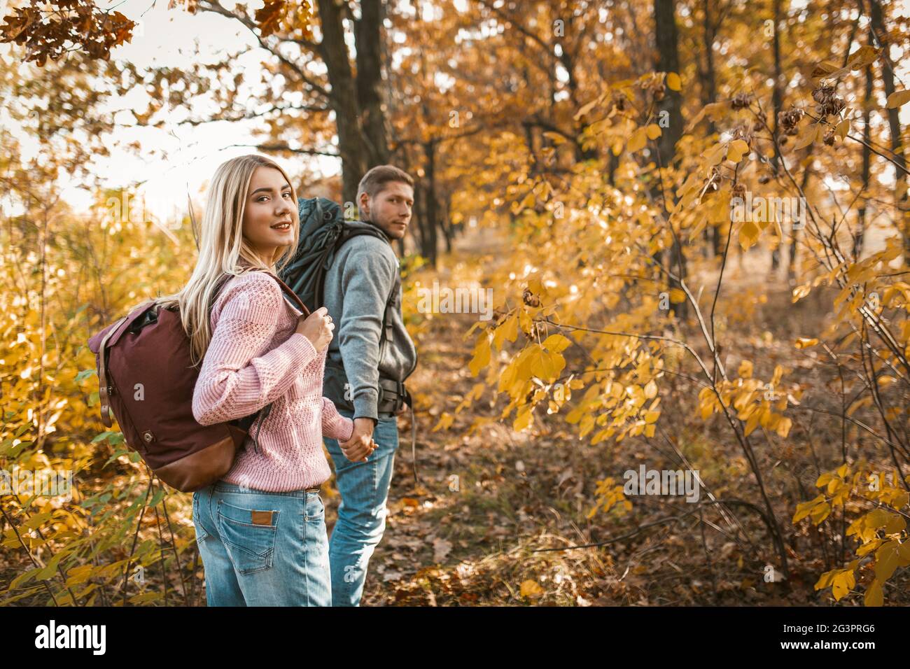 Un couple souriant de touristes marchant le long d'un chemin forestier tenant les mains et regardant en arrière la caméra Banque D'Images