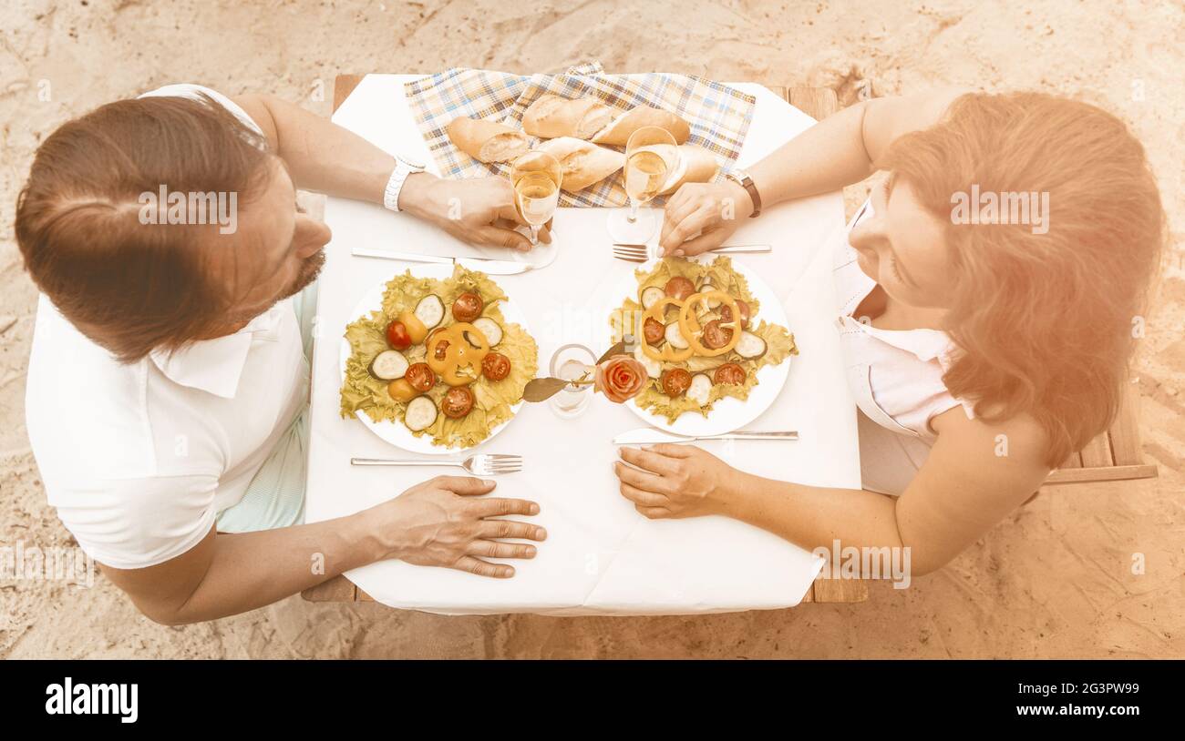 Couple amoureux de la vue en grand angle assis à une table sur une plage de sable Banque D'Images
