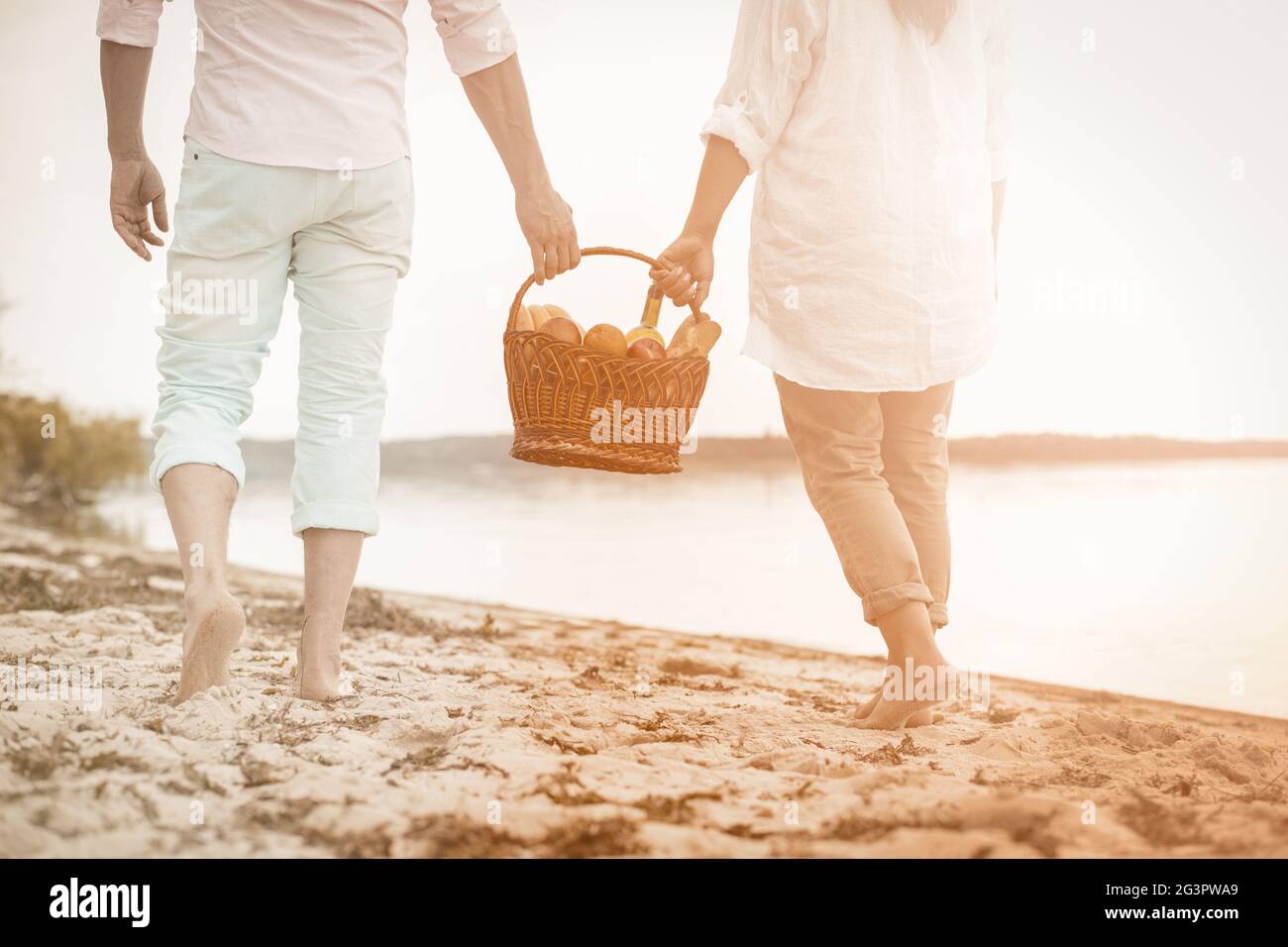 Un couple adulte marche le long de la mer en tenant un panier de nourriture Banque D'Images