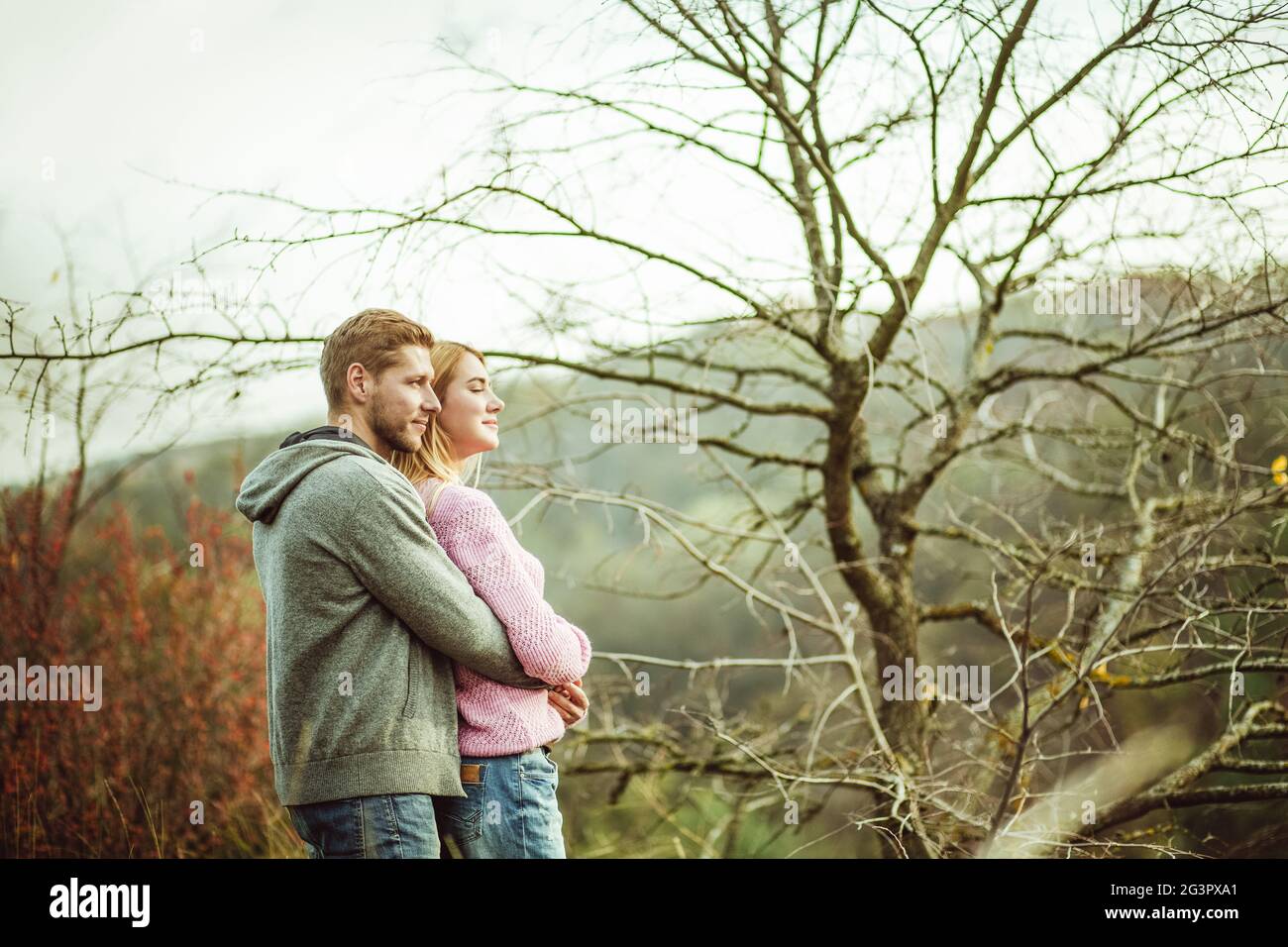 Un couple envoûté se dresse au sommet de la colline en admirant le coucher du soleil. Sur le fond d'un arbre sans feuilles. Concert d'ambiance d'automne Banque D'Images