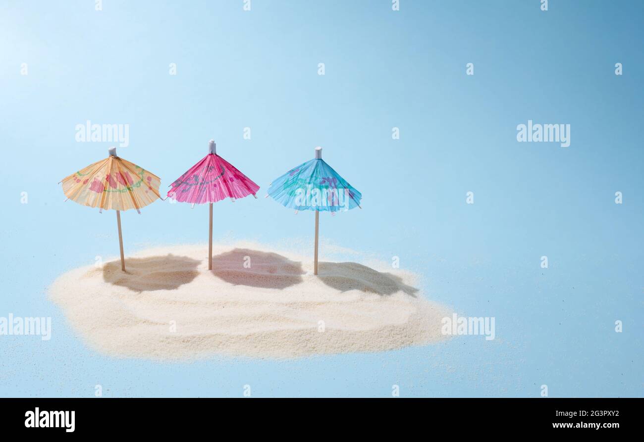 Trois parasols colorés sur l'île de sable au soleil sur un fond bleu, un été plage de vacances et de Voyage concept, gros plan. Banque D'Images