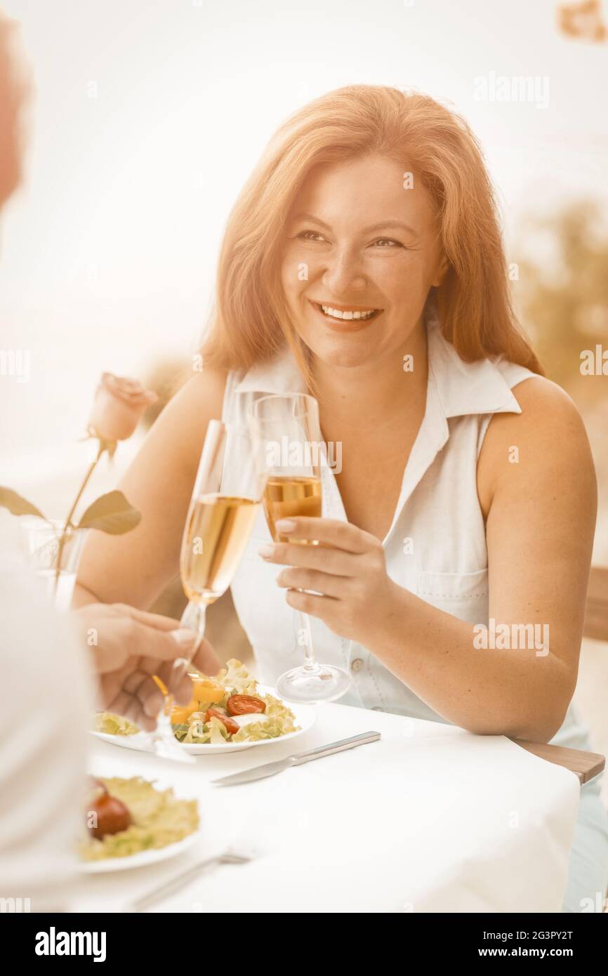 Une femme heureuse tient un verre de vin blanc souriant tout en regardant son mari. Un couple caucasien mature célèbre un anniversaire de mariage Banque D'Images